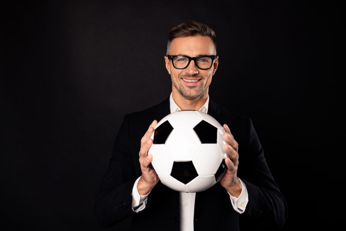 homme souriant en costume tenant un ballon de football