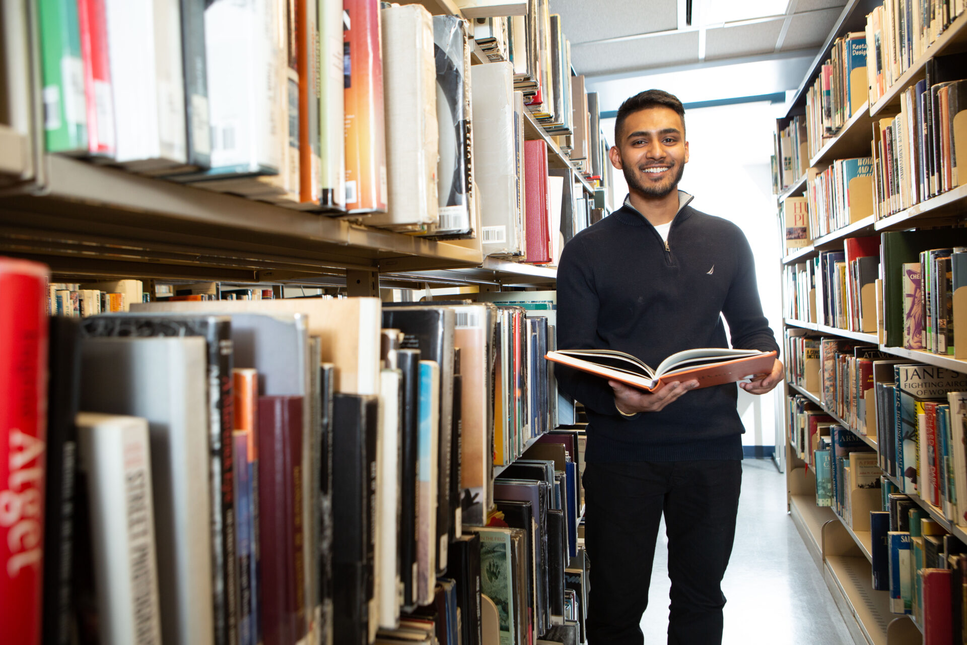 étudiant debout parmi les étagères de la bibliothèque, livre en main