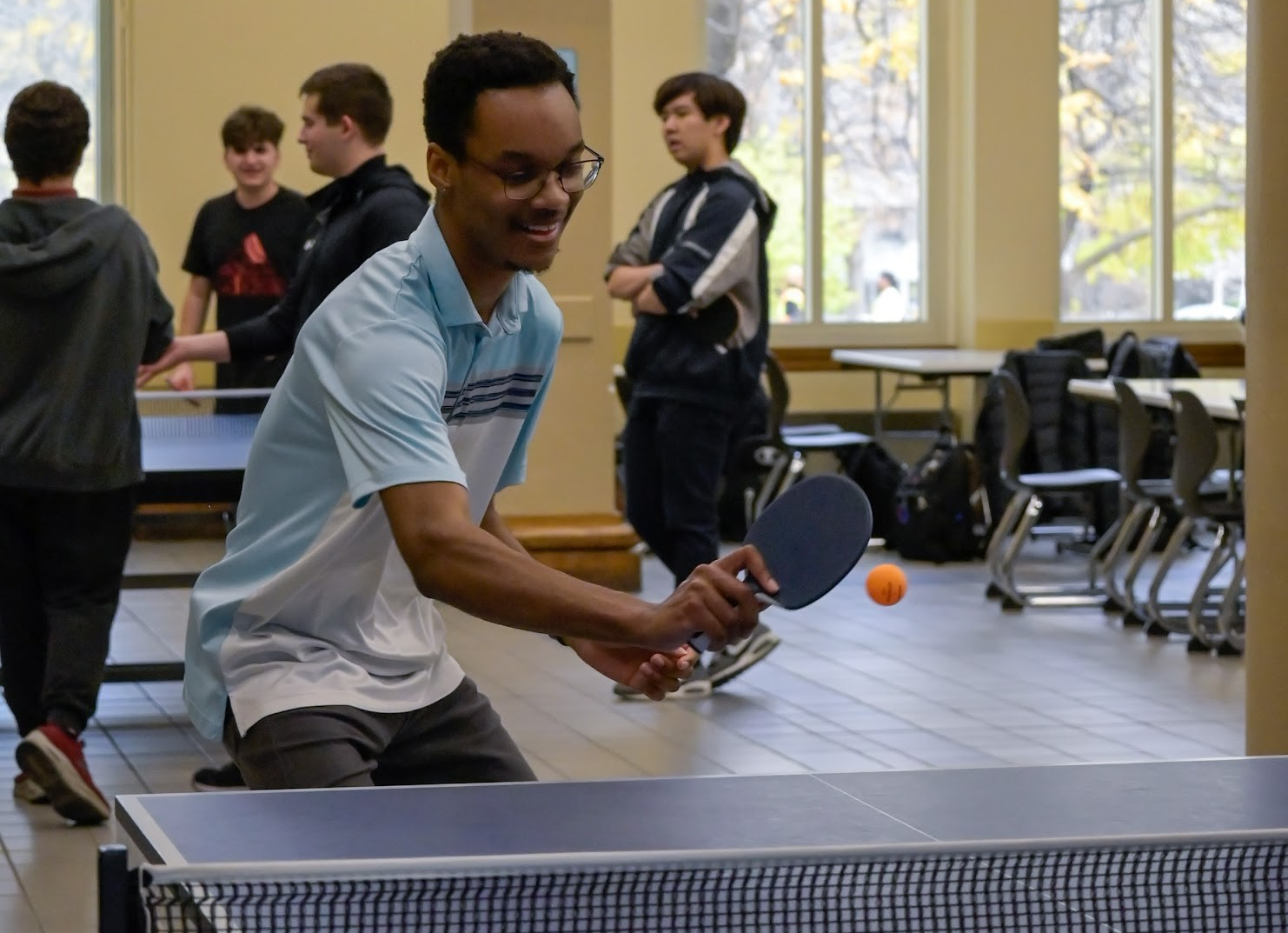 un étudiant souriant renvoyant une balle de ping-pong à un adversaire invisible